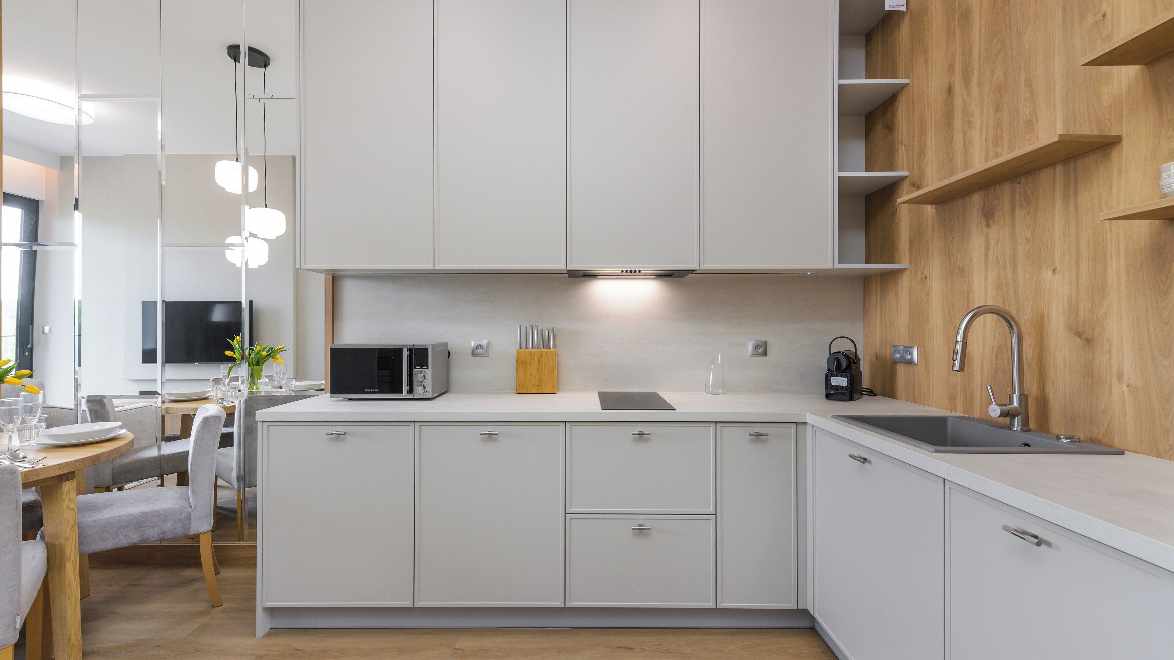 A modern kitchen with white cabinetry, a built-in microwave, a wooden shelf, and a sleek faucet.