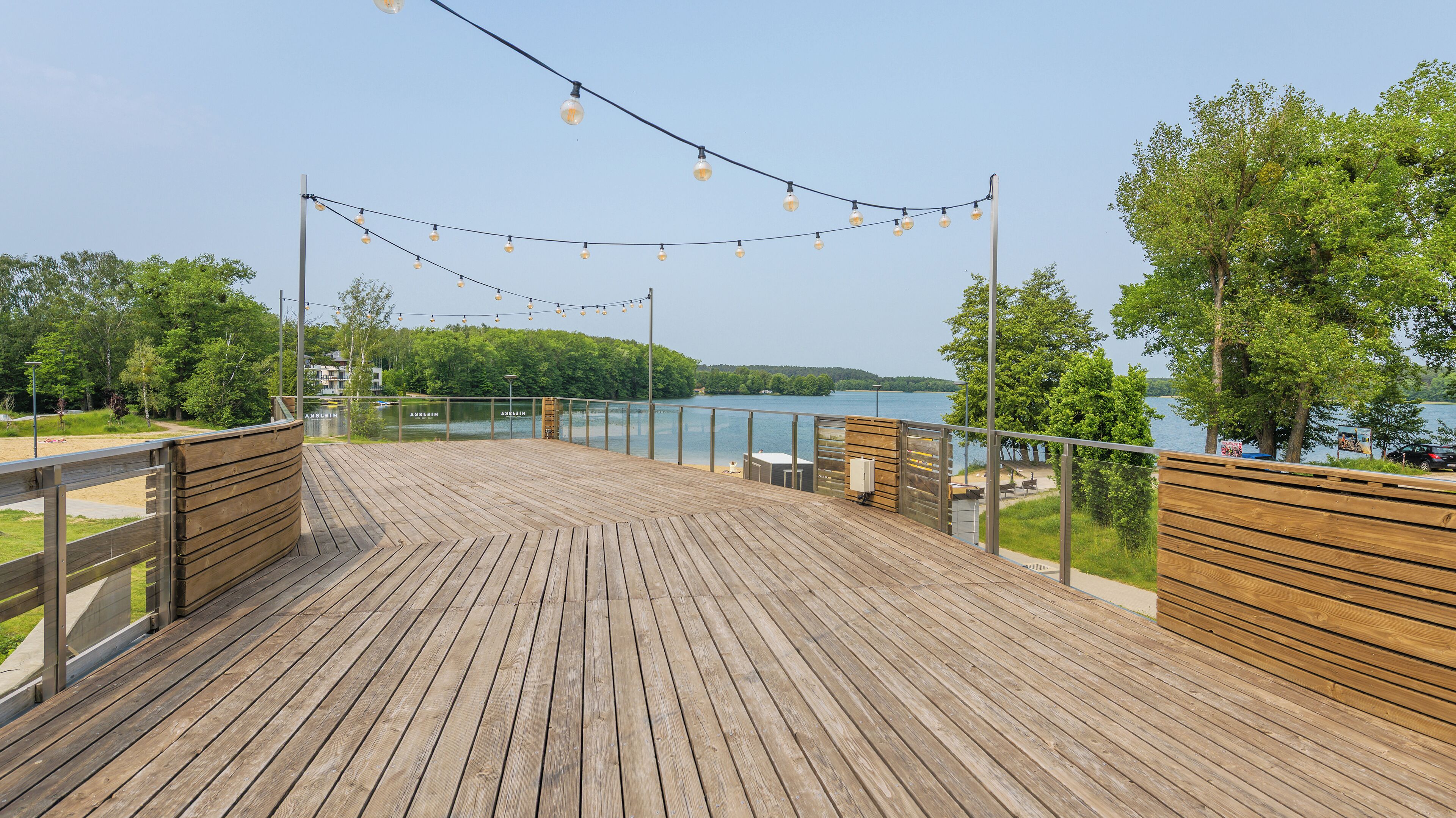Eine Holzterrasse mit Lichterketten, mit Blick auf einen See, umgeben von einem Holzzaun und Bänken.