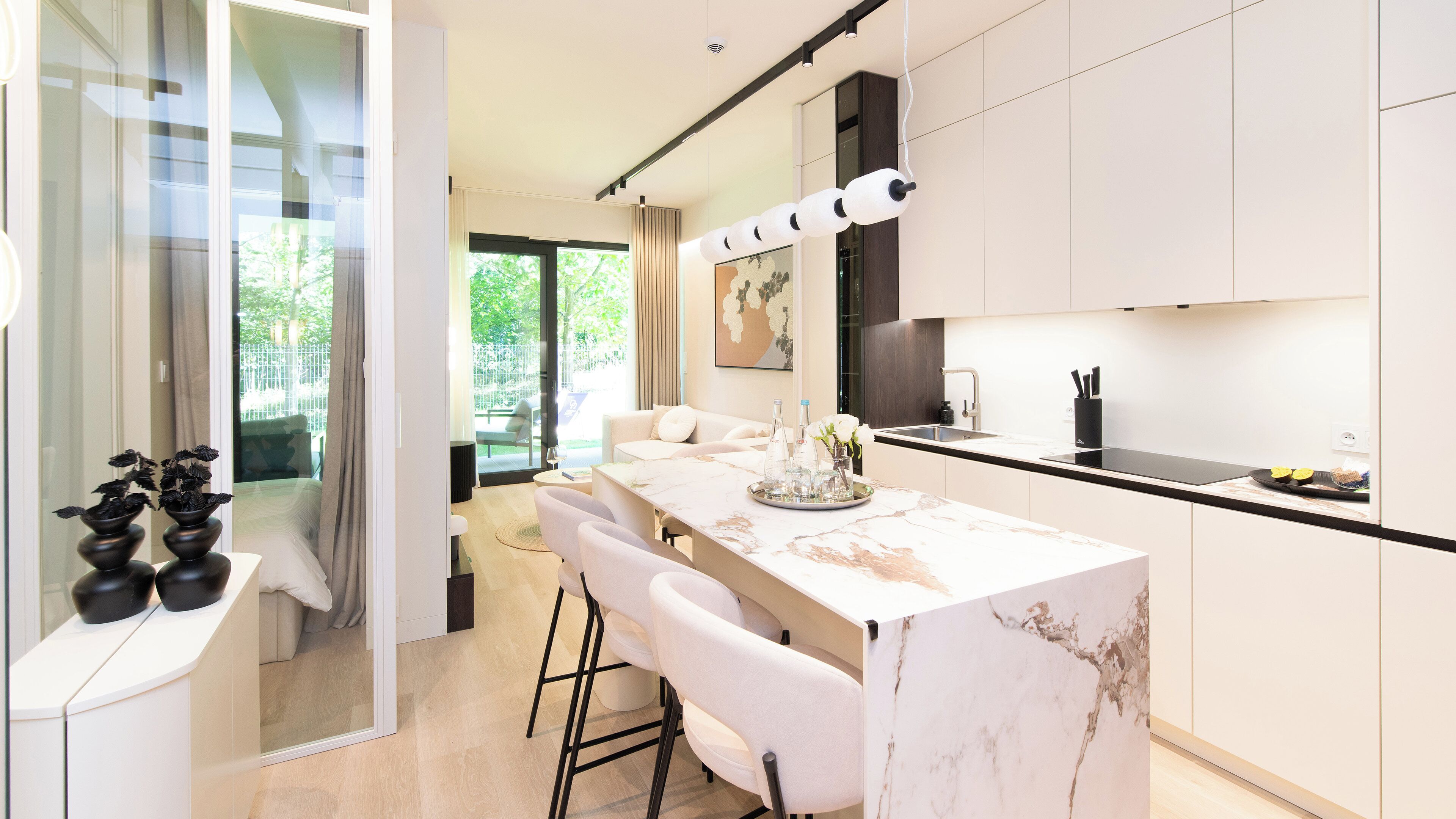 A modern kitchen with a marble countertop, a dining area with white chairs, and a view of the outdoors.