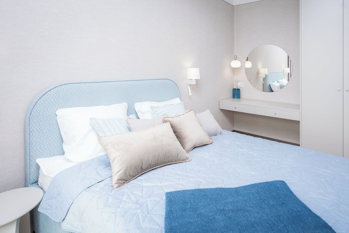 Un lit avec une couette bleue, une table de chevet, un miroir et une petite table.