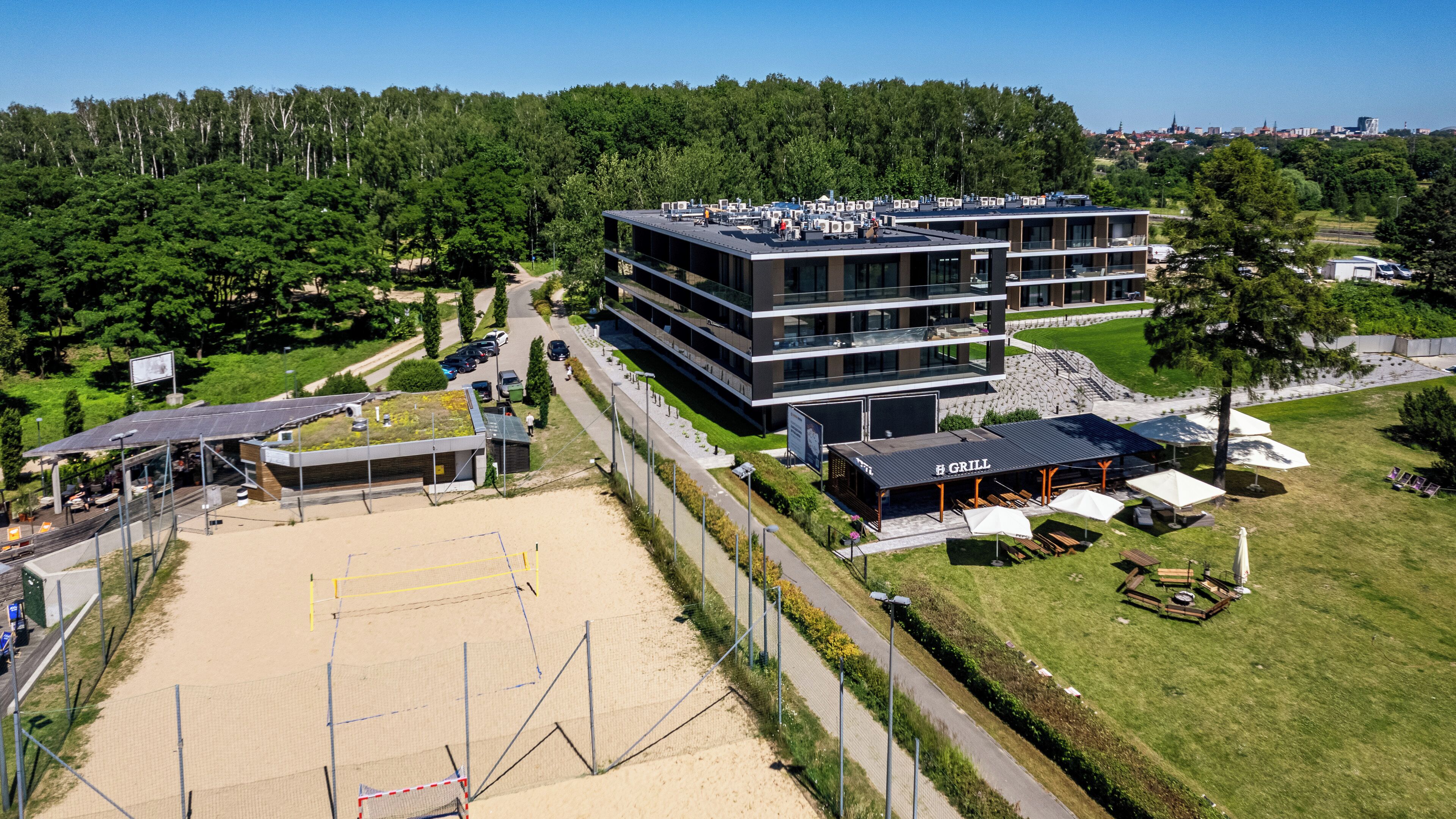 A modern hotel with multiple floors, outdoor seating, and a sports field.
