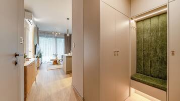 A modern hallway with a wooden floor, a green upholstered bench, and a view into a room with a large window and a dining area.