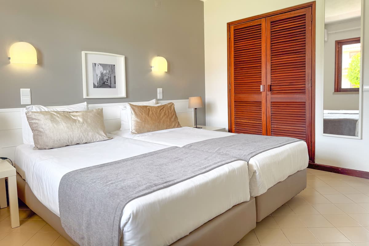 Una cama doble con dos almohadas, una mesita de noche, una lámpara, un cuadro en la pared y un armario de madera.