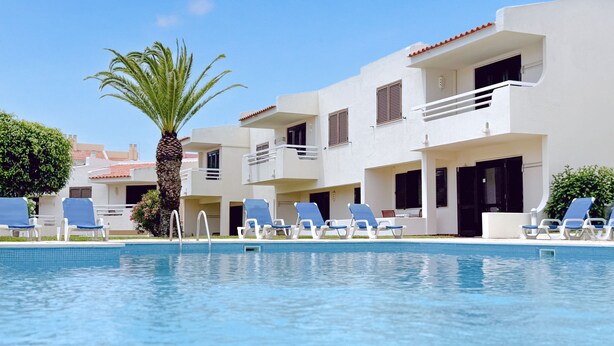 A poolside area with multiple lounge chairs and a palm tree. - Aura Village City Beach Apartments (Albufeira)