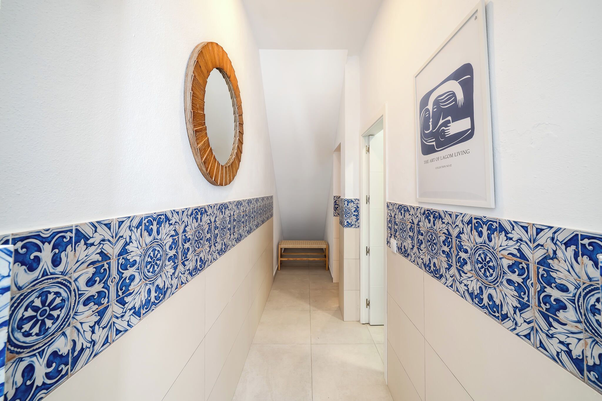 Un pasillo con baldosas de diseño azul y blanco, un banco de madera y una obra de arte enmarcada en la pared.