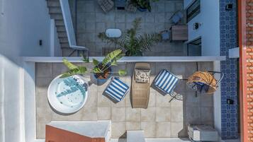 A rooftop patio with a hot tub, lounge chairs, and potted plants.