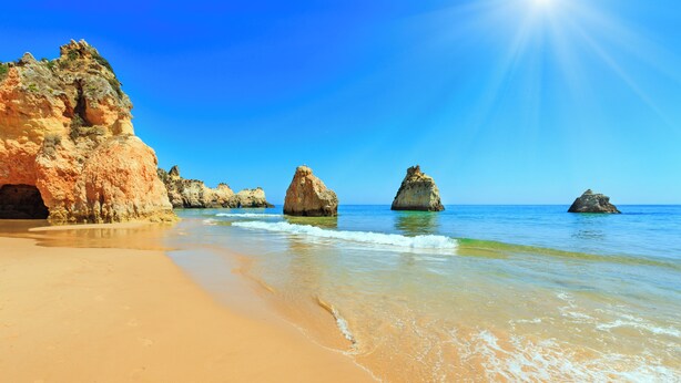 Una playa con aguas azules cristalinas, una orilla arenosa y grandes formaciones rocosas.