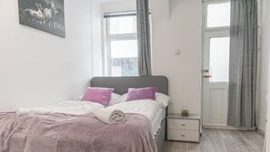 Quarto com uma cama, mesa de cabeceira, janela e porta.