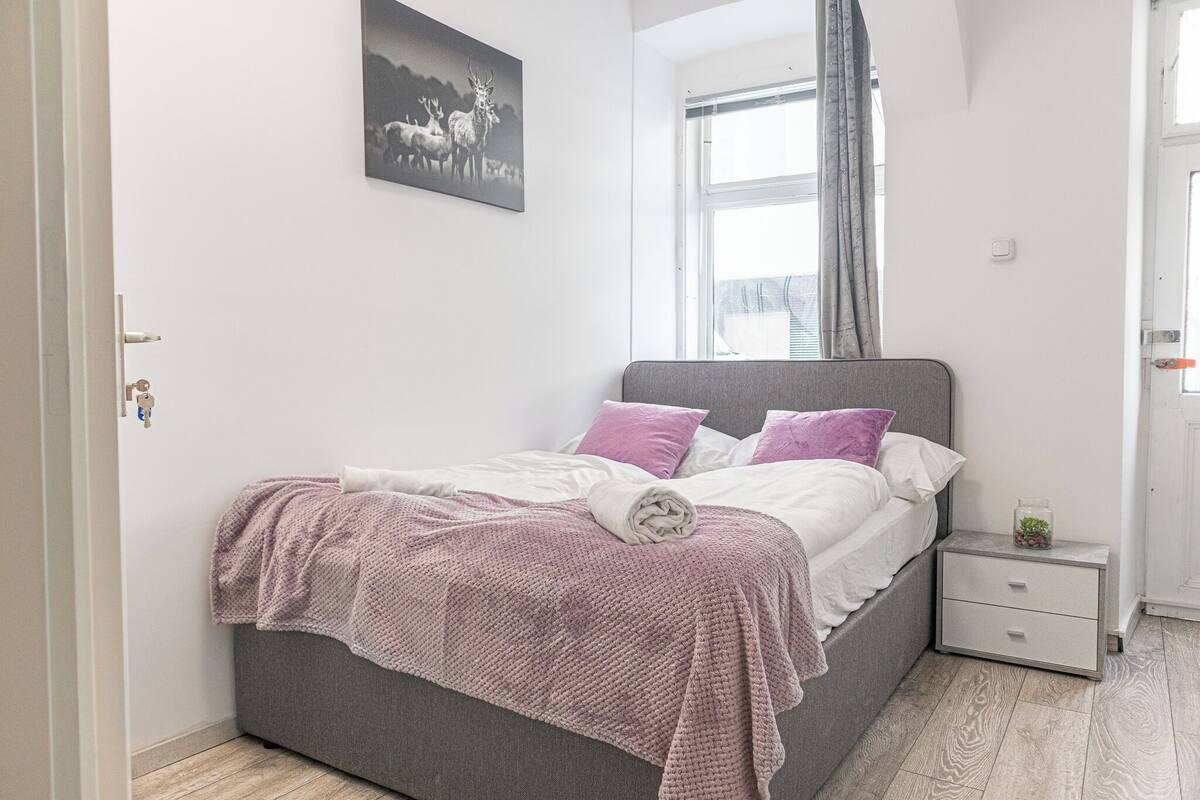 A bedroom with a bed, a nightstand, a window, and a door.