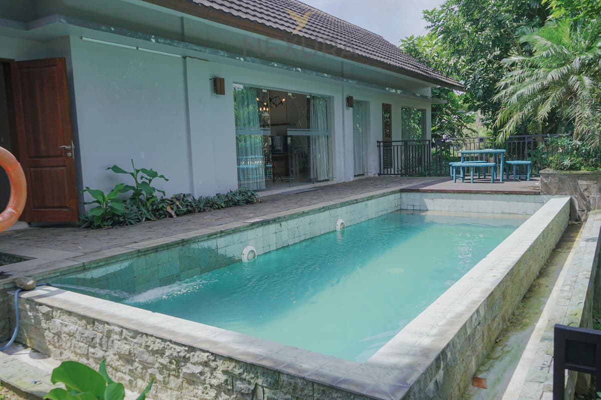 Une piscine bordée de pierres, une porte en bois et un petit espace patio avec une table et des chaises.