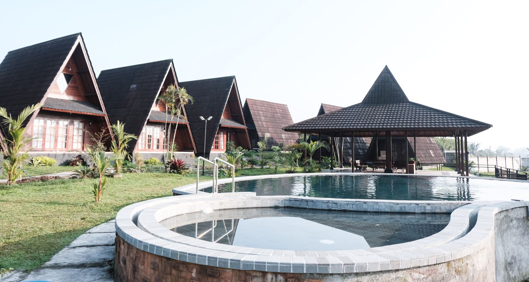 Un resort con varias construcciones tipo bungalow, una piscina central y un pabellón.
