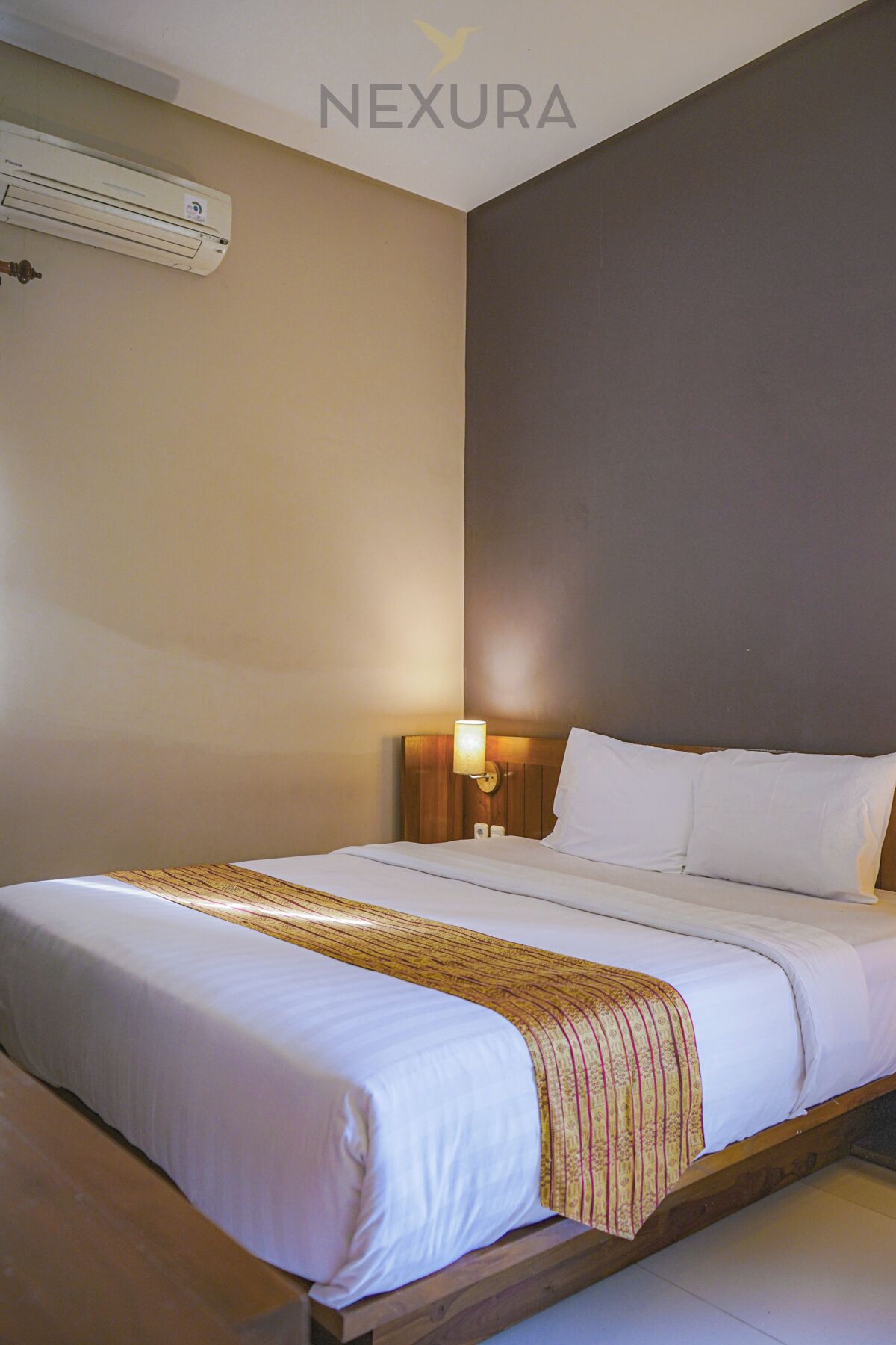 A hotel room with a bed, a nightstand, a lamp, and an air conditioning unit.