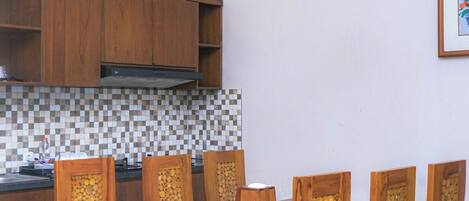 A dining area with a wooden table and chairs, a kitchen with wooden cabinets, and a tiled backsplash.