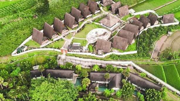 An aerial view of a resort with multiple bungalow-style buildings, a central circular structure, and a surrounding water body. - Jambu Klutuk Resort (Parakan)