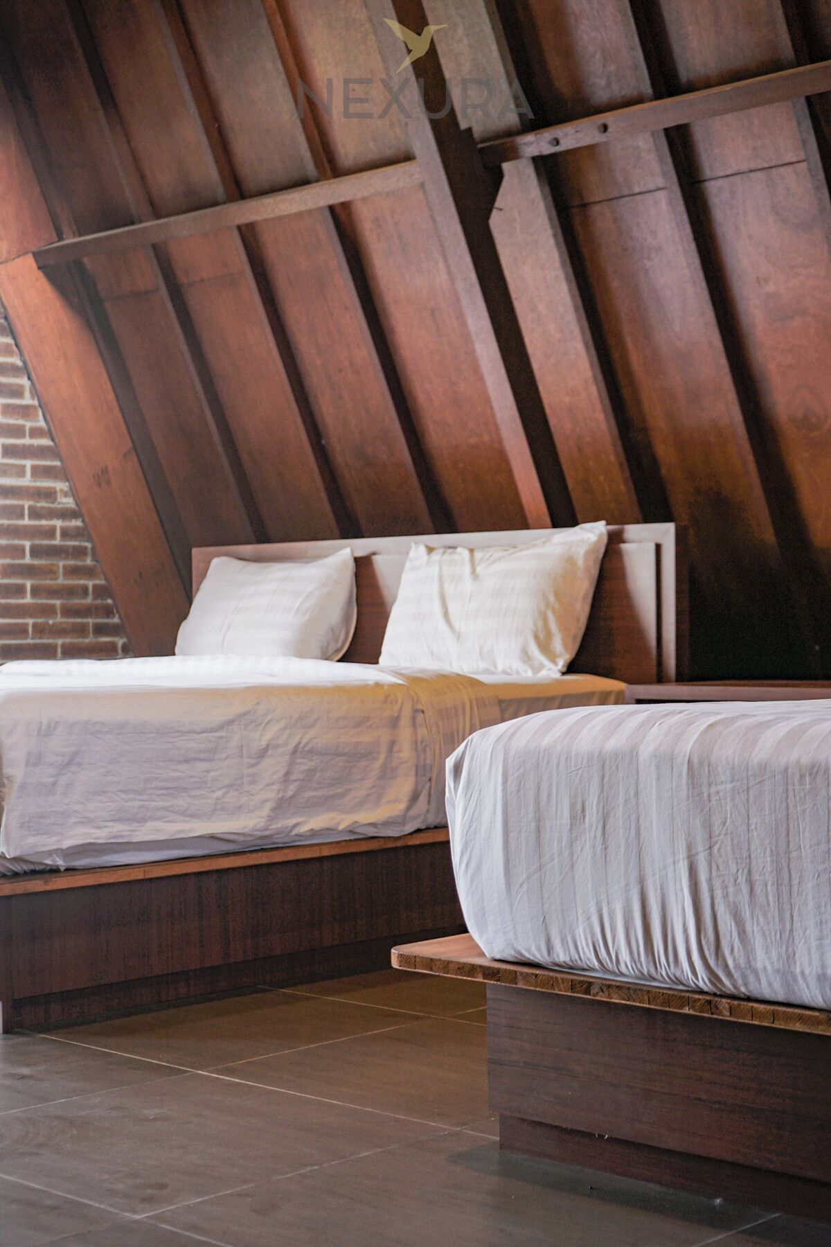 A bedroom with two beds, wooden headboard, and a brick wall.