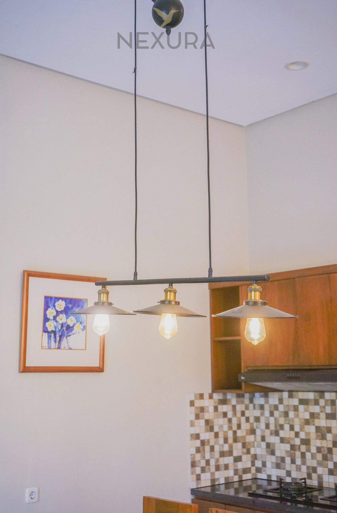 Una cocina con lámparas colgantes, un cuadro enmarcado y un salpicadero de azulejos.