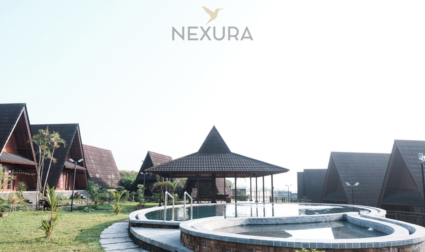 A modern resort with a central pool, surrounded by unique architecture and a clear sky.