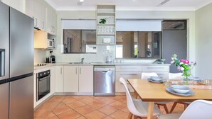 Een moderne keuken met witte kastjes, roestvrijstalen apparatuur en een eethoek met een houten tafel en witte stoelen.