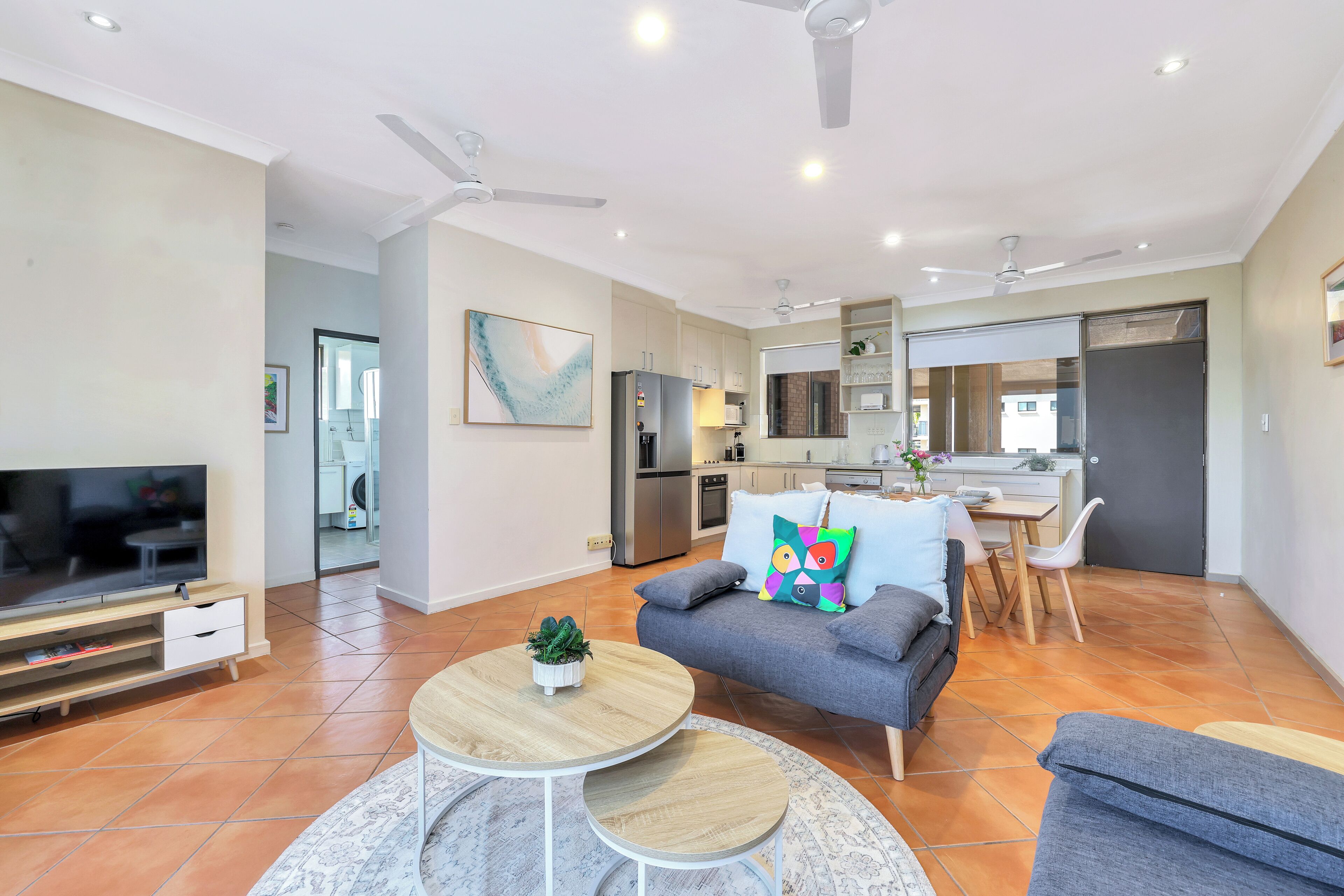 A modern living room with a grey sofa, a TV, and a dining area with a table and chairs.