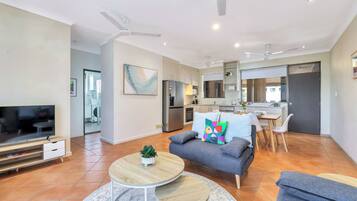 A modern living room with a grey sofa, a TV, and a dining area with a table and chairs.