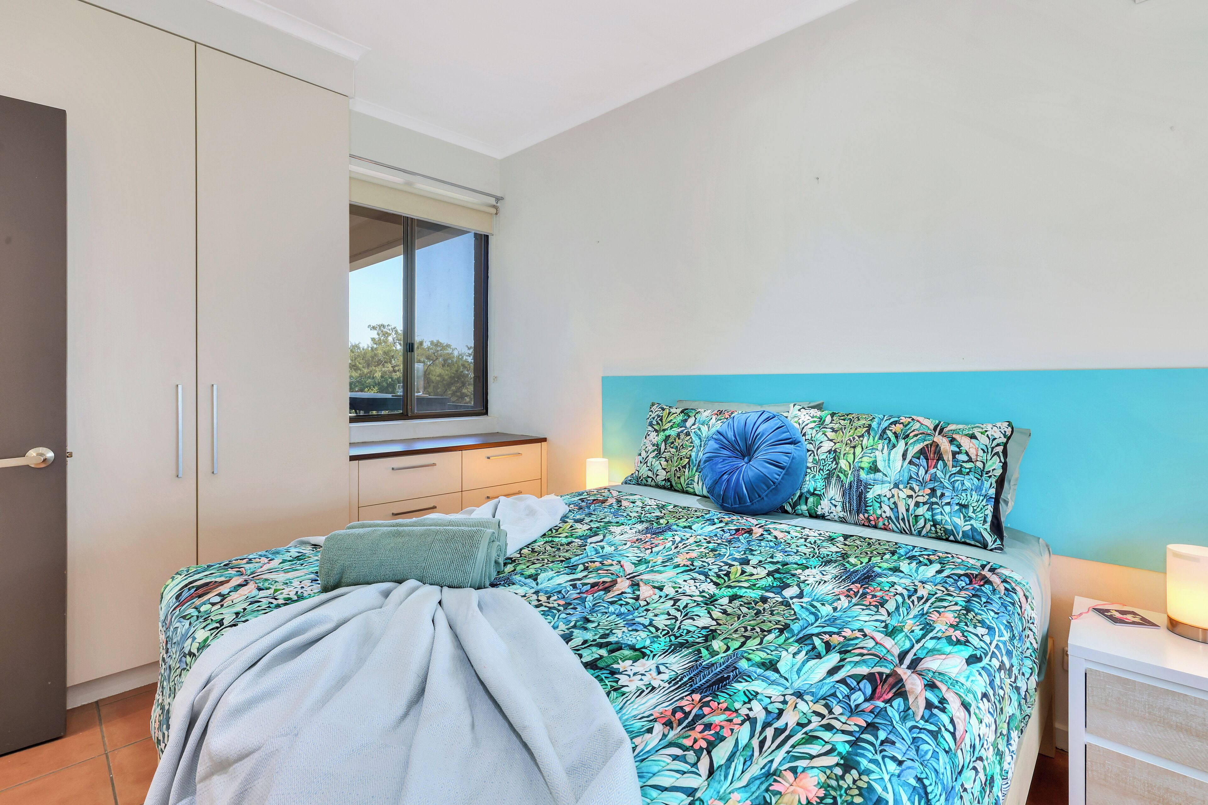 A bedroom with a bed, a window, a wardrobe, and a nightstand.