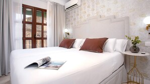 A hotel room with a large bed, a small bedside table with a lamp, an air conditioning unit, and a window with curtains. - Cozy 2bd Apartment in Seville. Conde de Ibarra IV (Seville)