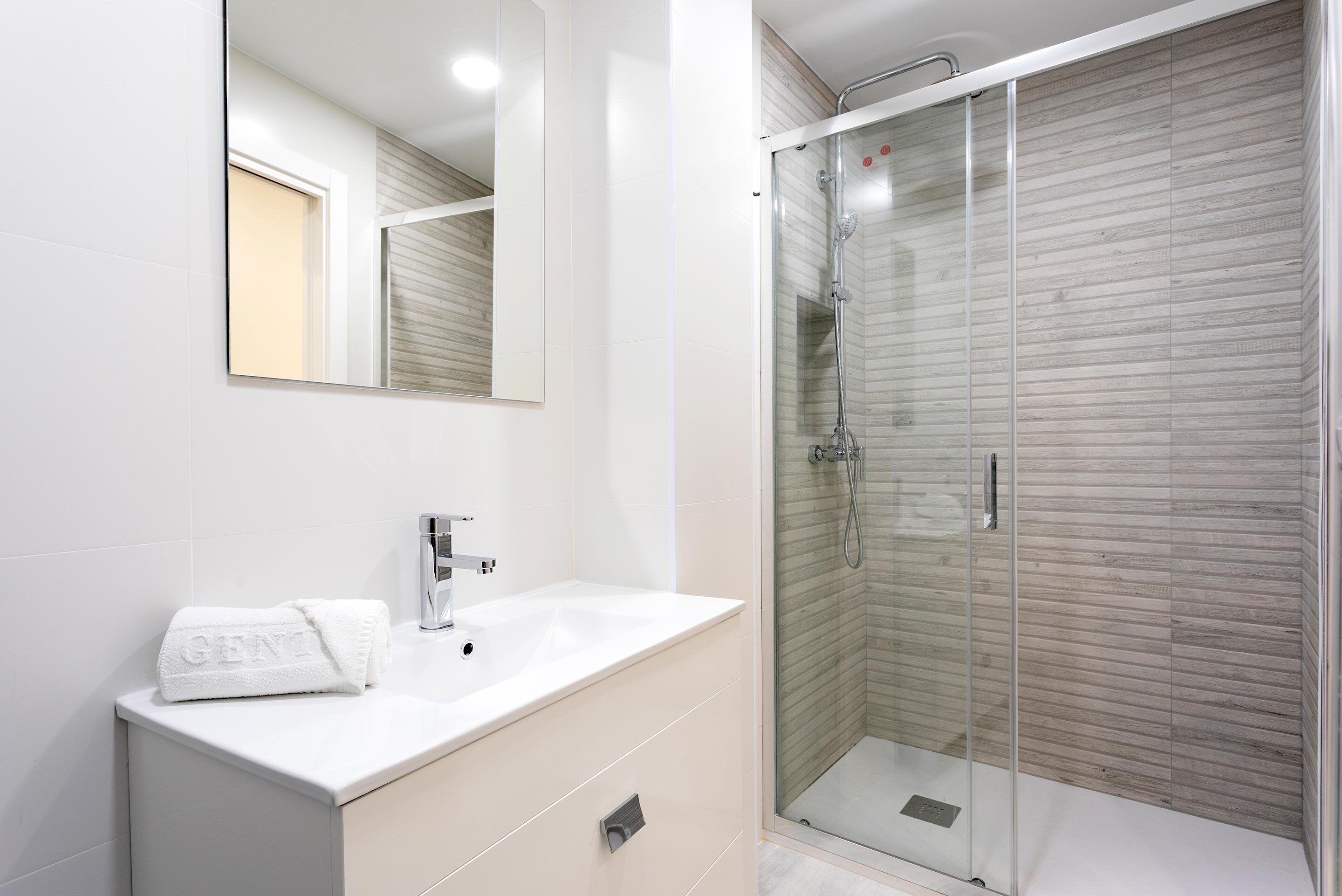 A modern bathroom with a white vanity, a glass shower enclosure, and a large mirror.