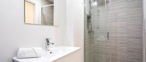A modern bathroom with a white vanity, a glass shower enclosure, and a large mirror.