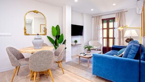 A modern living room with a blue sofa, a dining table with chairs, a large mirror, and a television. - Cozy 2bd Apartment in Seville. Conde de Ibarra IV (Seville)
