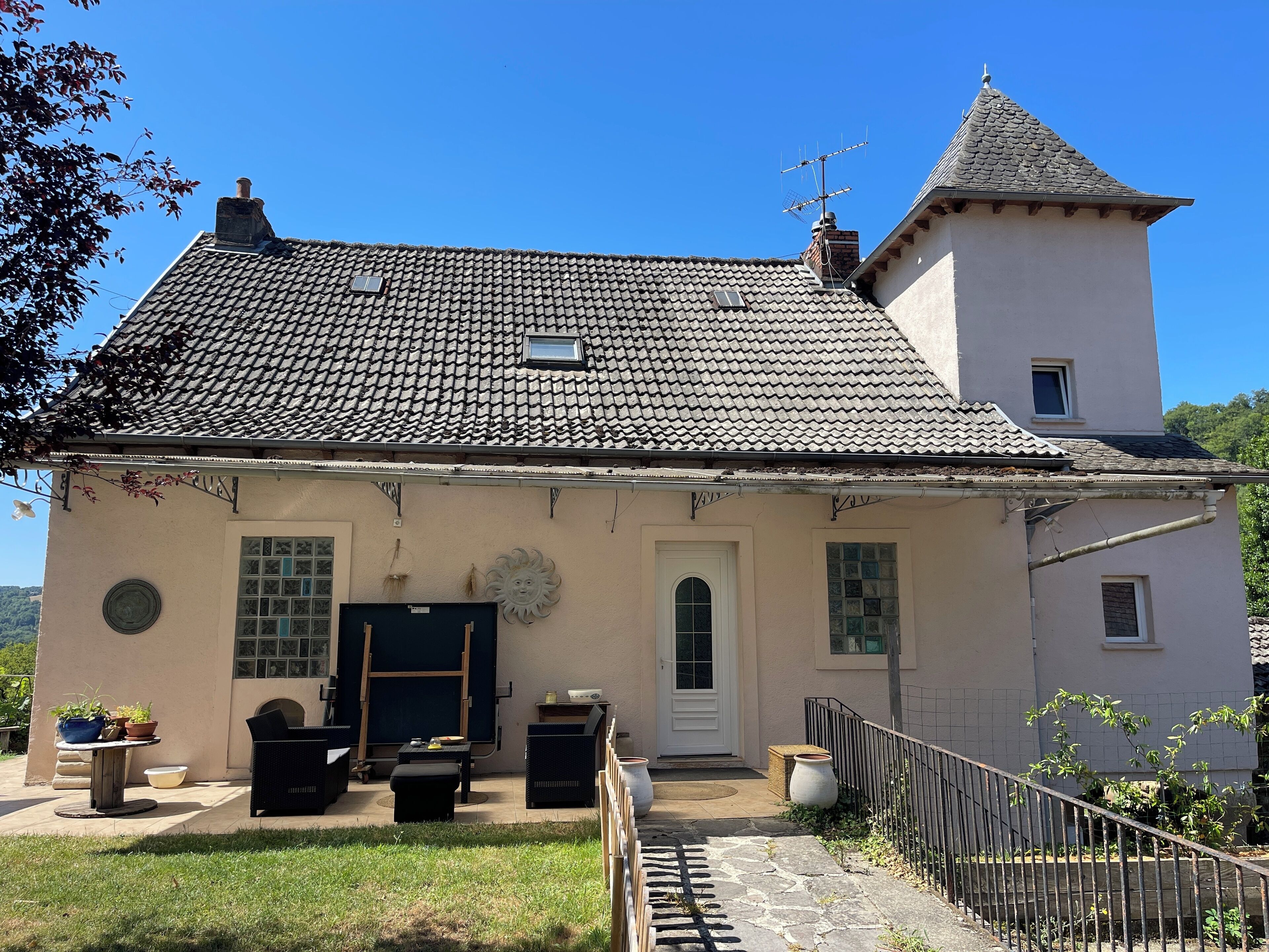 A two-story house with a tiled roof, a small tower, and a front door.
