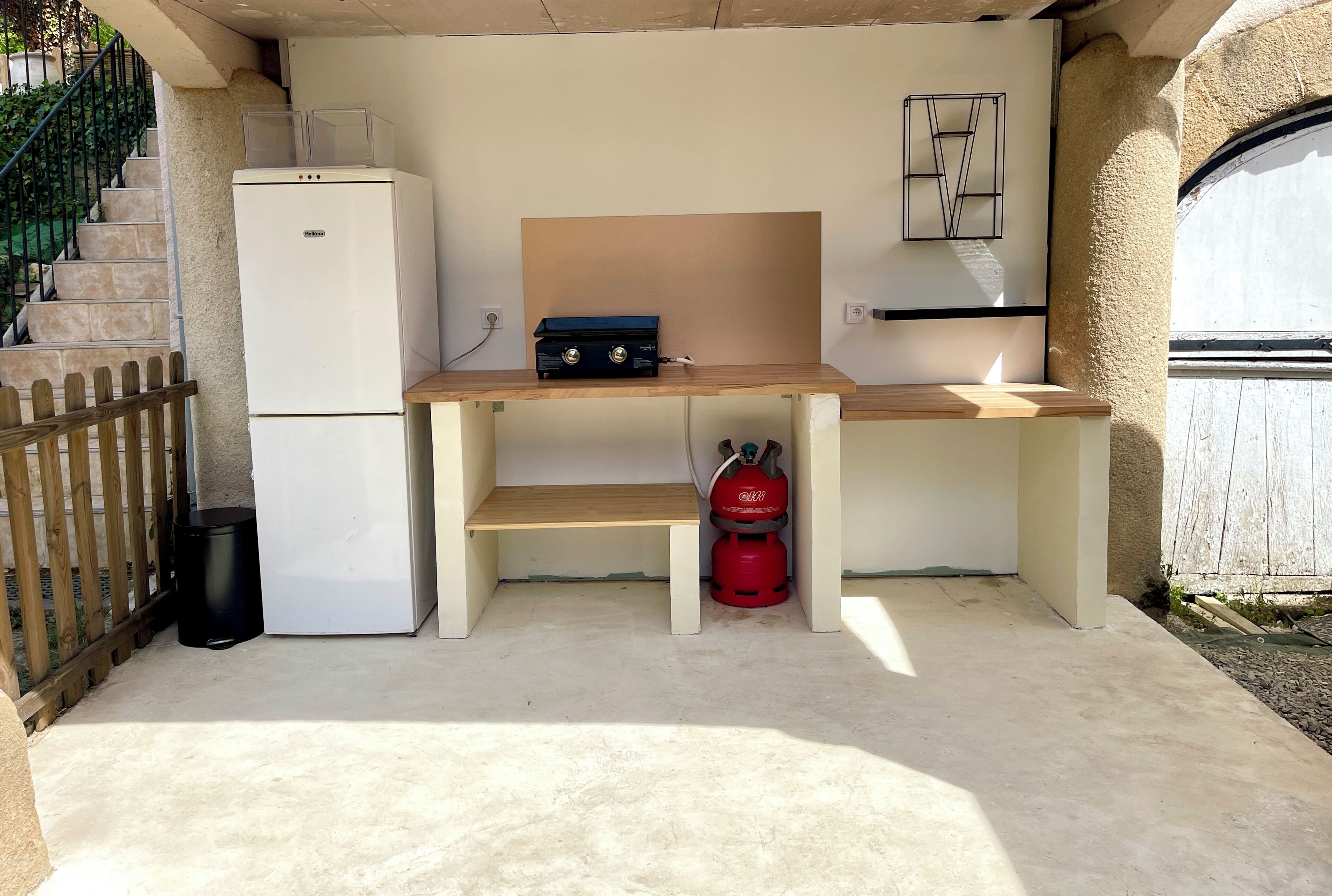 A compact kitchen area with a white refrigerator, a wooden countertop, and a red gas cylinder.