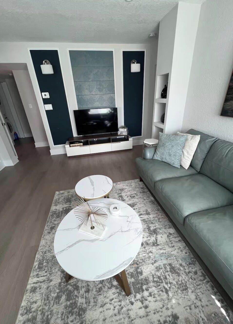 Ein Wohnzimmer mit grauem Sofa, einem weißen Couchtisch, einem Fernseher und einem gemusterten Teppich.