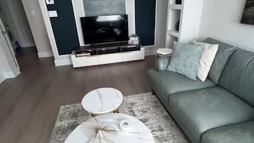 A living room with a grey sofa, a white coffee table, a TV, and a patterned rug.