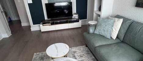 Ein Wohnzimmer mit grauem Sofa, einem weißen Couchtisch, einem Fernseher und einem gemusterten Teppich.