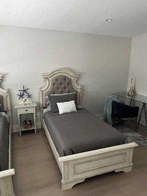 A bedroom with a large bed, a bedside table, a chair, and a small table with decorative items.