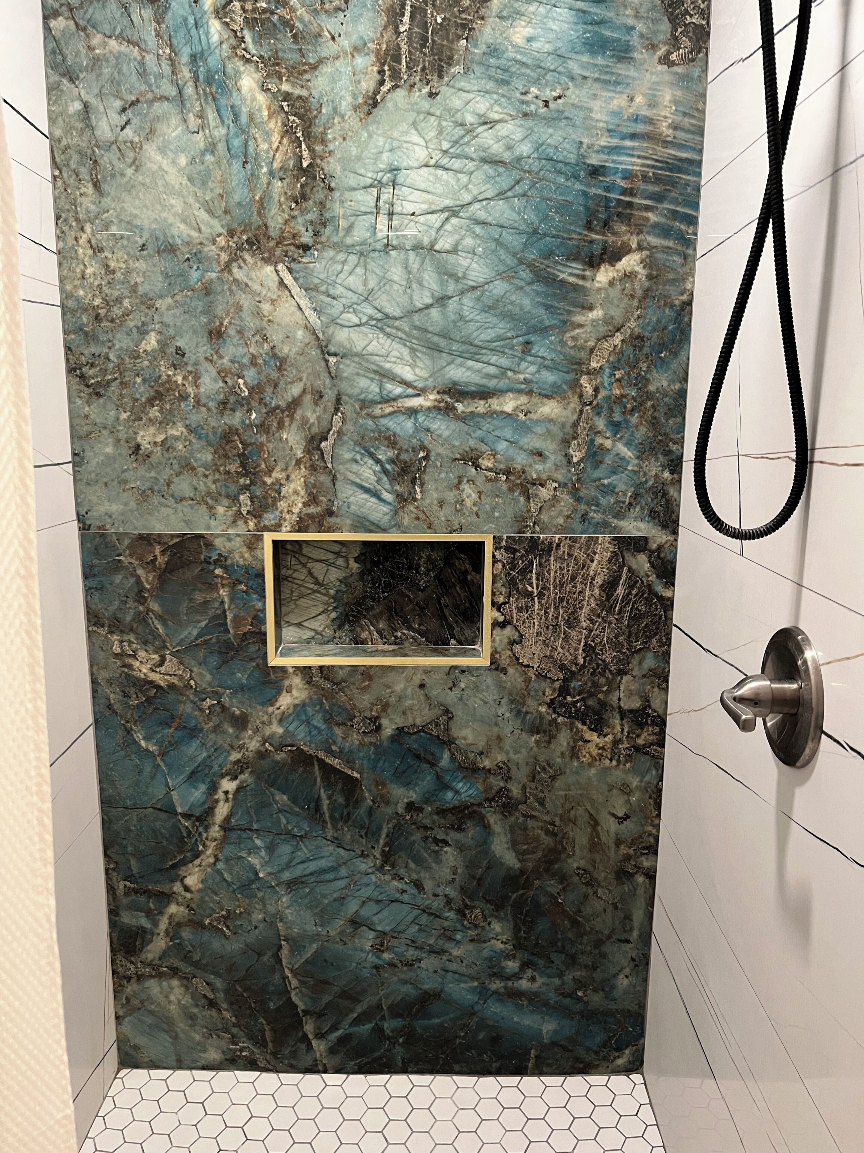 A bathroom with a marble wall, a framed picture, and a towel rack.