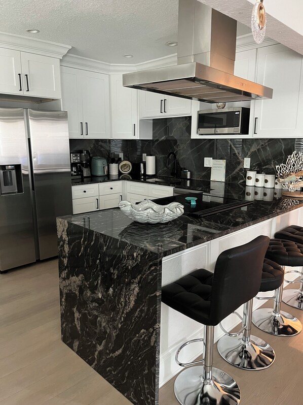 A modern kitchen with a marble island, stainless steel appliances, and black bar stools.