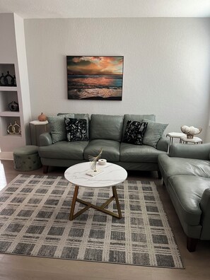 A living room with a sectional sofa, a round coffee table, and a painting on the wall.