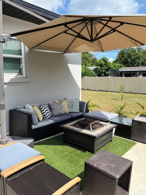 An outdoor patio area with a sectional sofa, a fire pit, and outdoor furniture.