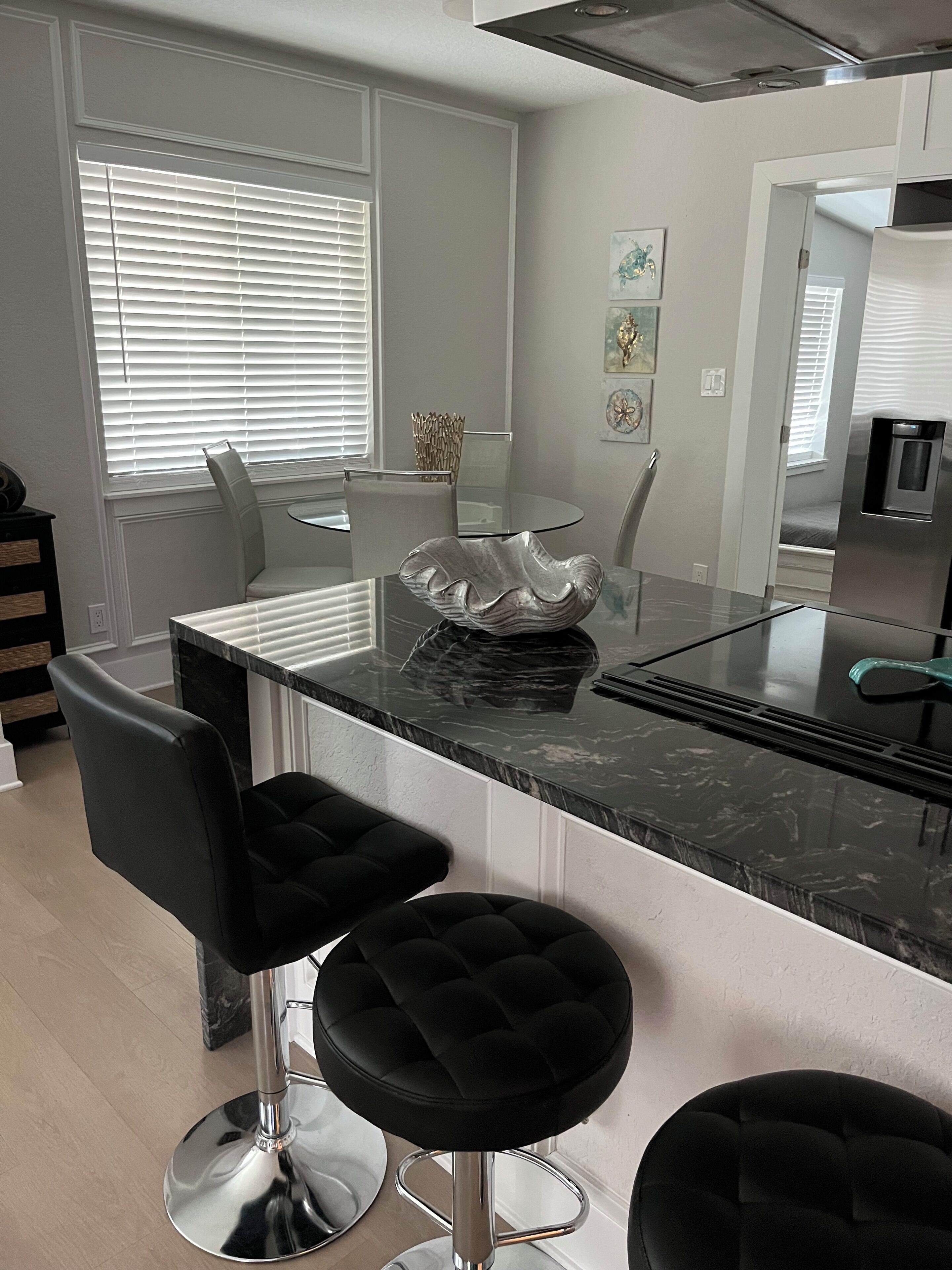 A modern kitchen with a central island, bar stools, and a dining area with a glass table.