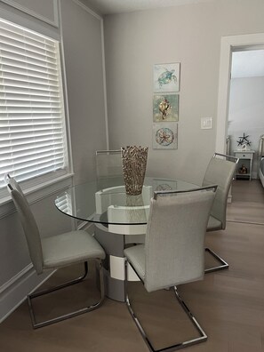 A dining area with a glass table surrounded by four grey chairs, a decorative metal vase, and wall art.