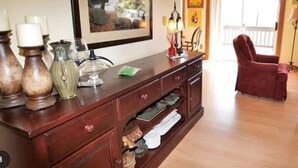 Ein Holzkonsolentisch mit Dekoration, ein gerahmtes Bild an der Wand und ein roter Sessel in einem Raum mit Holzdielen.