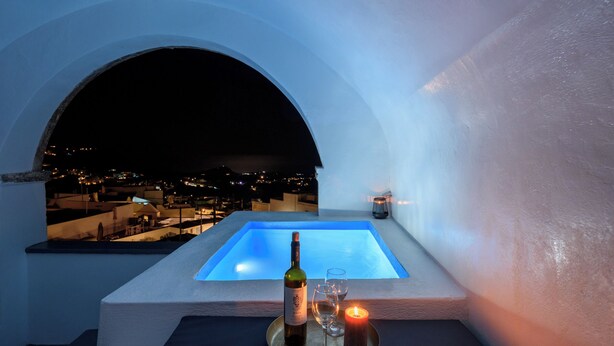 Terraza en la azotea con piscina, una botella de vino y copas sobre una bandeja, con vistas a un paisaje urbano nocturno.