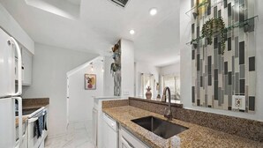 A modern kitchen with granite countertops, a stainless steel sink, and white cabinetry. - Bright 1-bedroom townhome near Texas Medical Center, NRG Stadium, and downtown. (Houston)