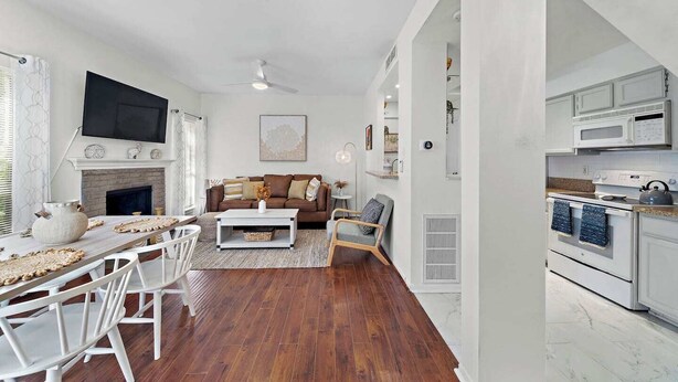 A modern living room with a fireplace, a flat-screen TV, and a dining area with a wooden table and white chairs. - Bright 1-bedroom townhome near Texas Medical Center, NRG Stadium, and downtown. (Houston)