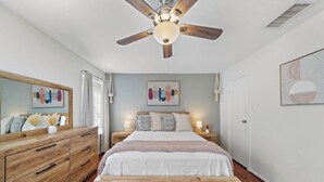 A bedroom with a wooden bed, a nightstand with a lamp, a ceiling fan, and artwork on the walls. - Bright 1-bedroom townhome near Texas Medical Center, NRG Stadium, and downtown. (Houston)