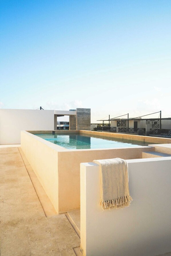 A rooftop pool with a clear view of the sky, a modern architectural design, and a seating area with a towel.