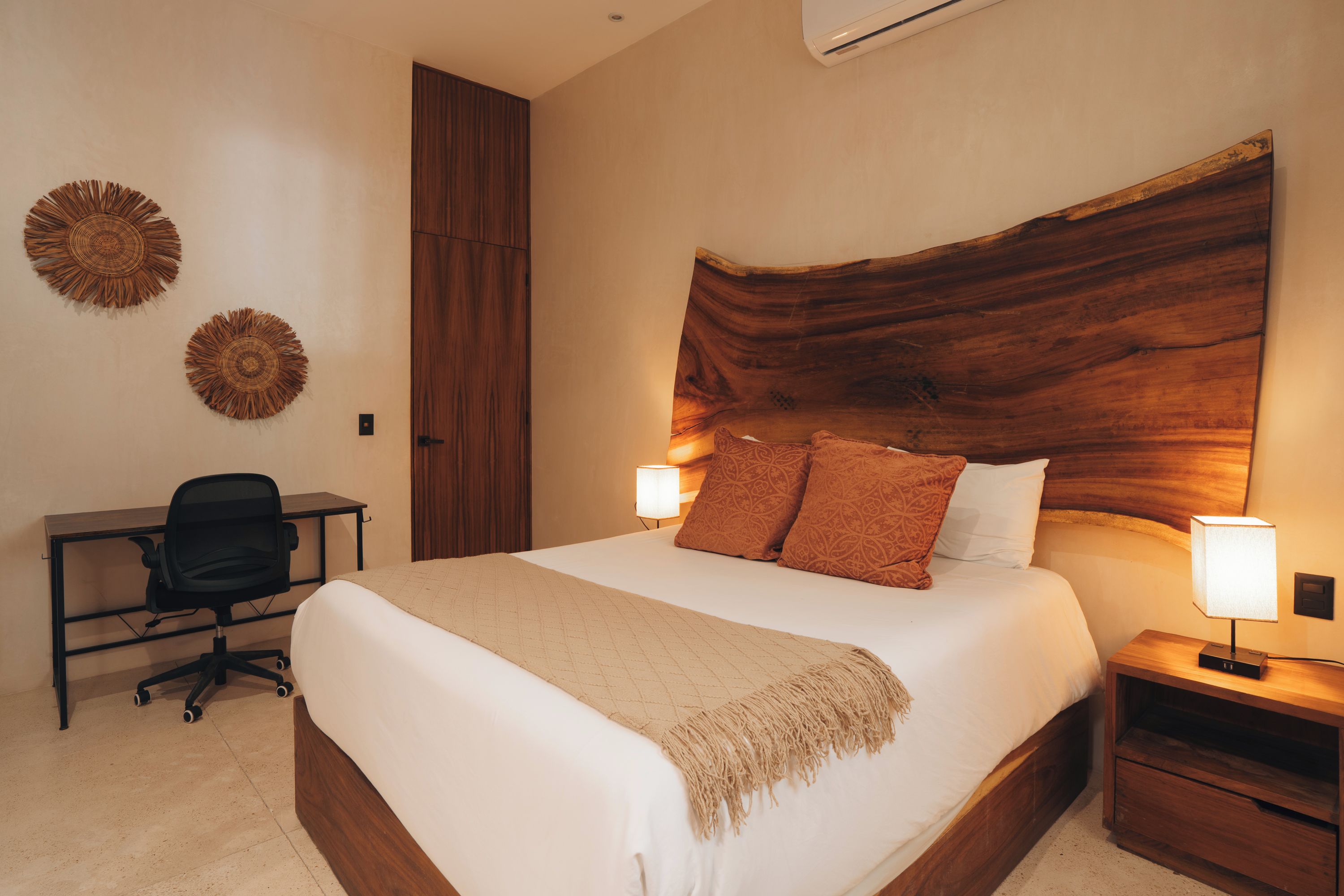 A hotel room with a large bed, two bedside lamps, a desk with a chair, and decorative wall art.
