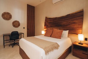 A hotel room with a large bed, two bedside lamps, a desk with a chair, and decorative wall art.
