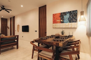 A modern dining area with a wooden table and chairs, a flat-screen TV mounted on the wall, and a painting above the table.